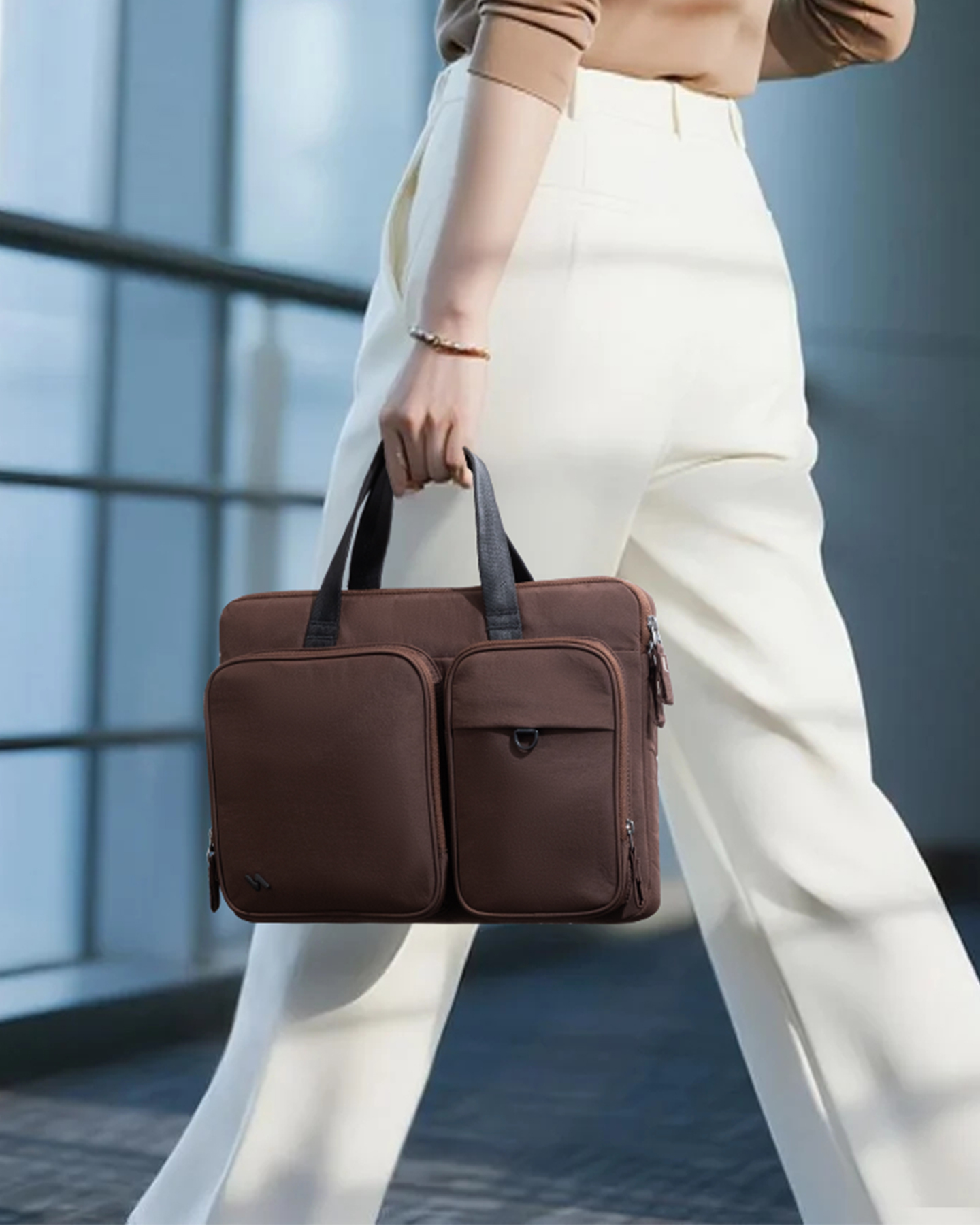 Eine Person in weißer Hose und beige farbenem Oberteil trägt eine braune Aktentasche mit zwei Vordertaschen.