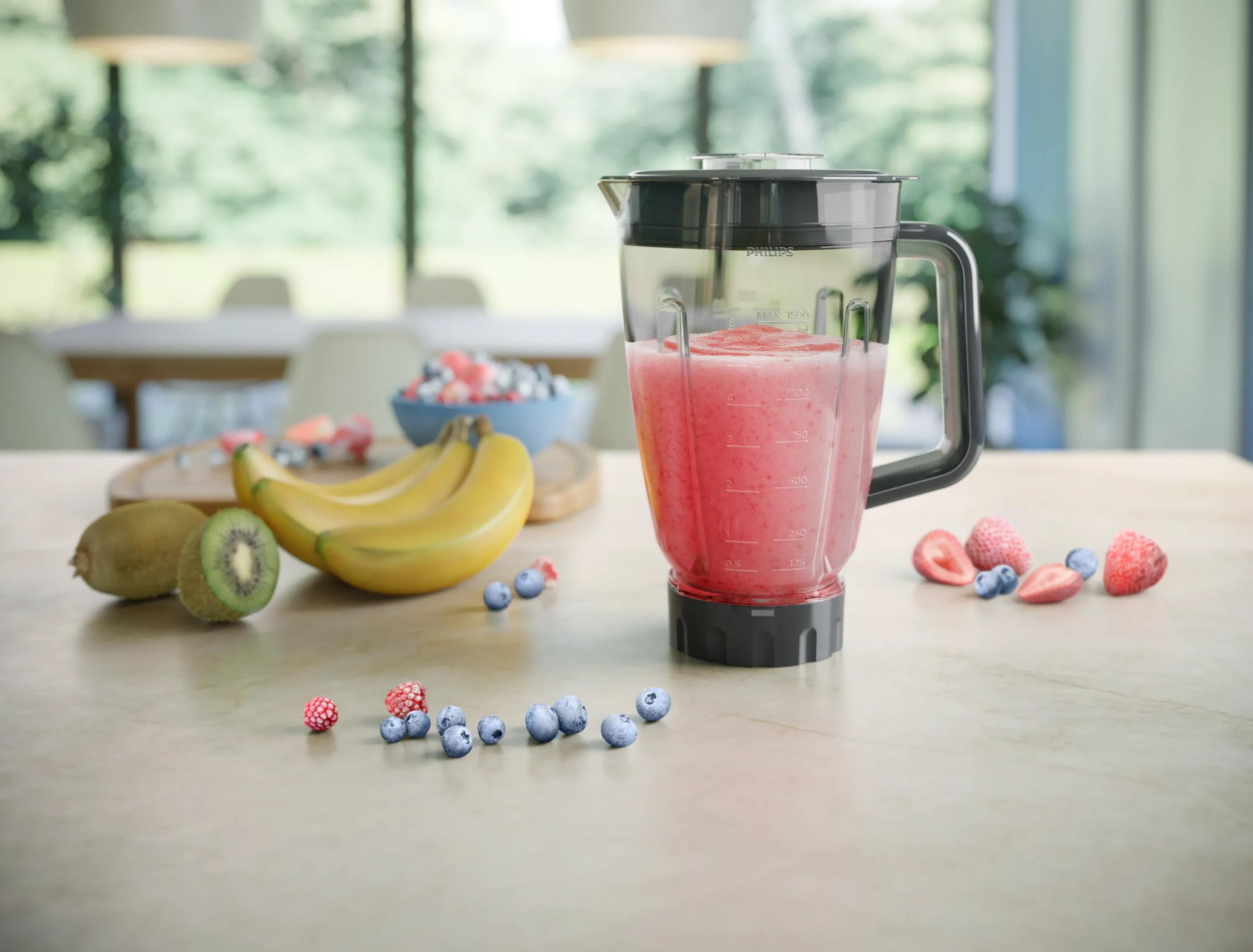 Blender z różowym smoothie stoi na blacie kuchennym, otoczony świezymi owocami, takimi jak banany, kiwi i jagody.