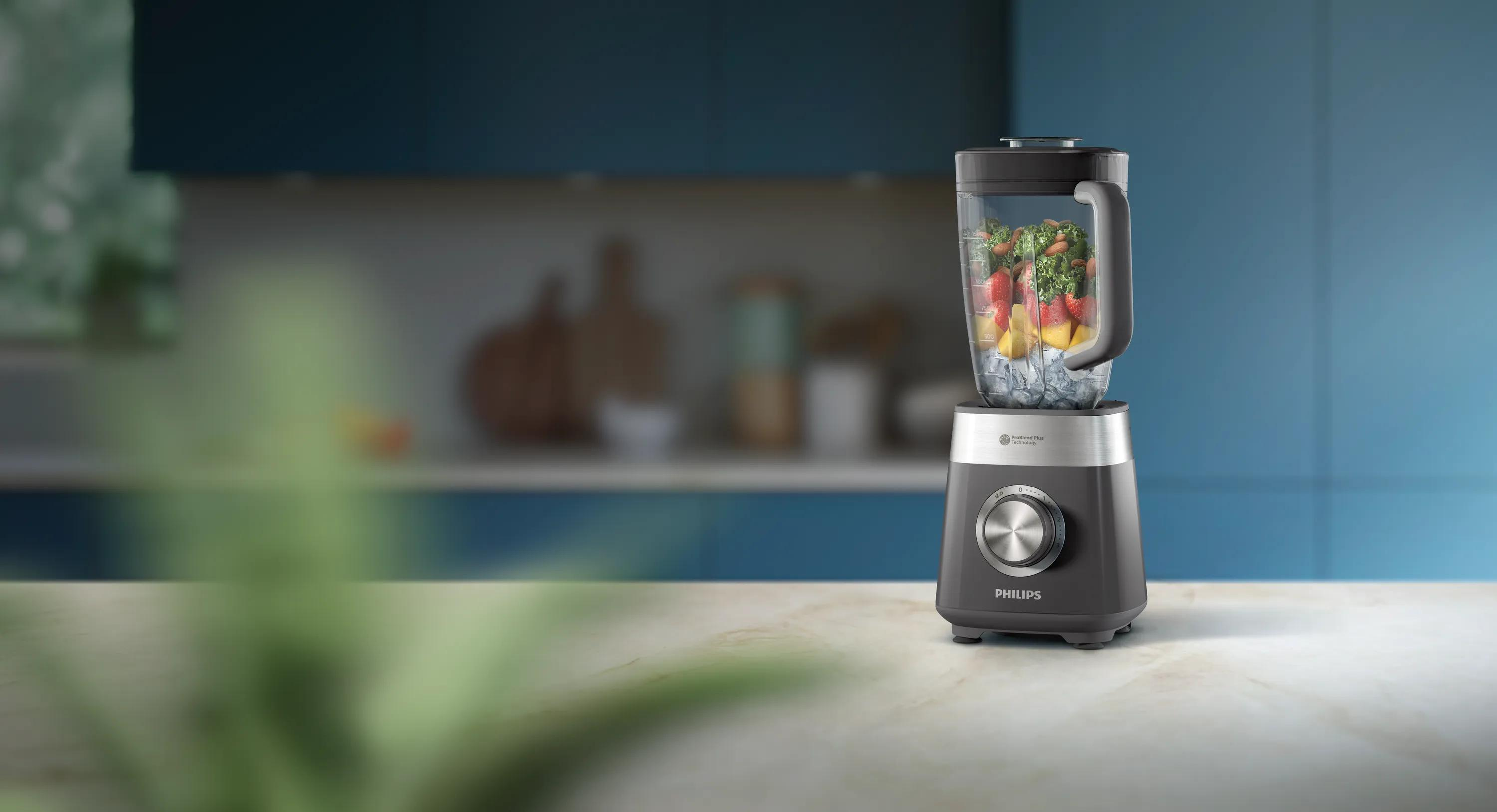 Szary blender Philips wypełniony owocami, warzywami i lodem stoi na blacie kuchennym.