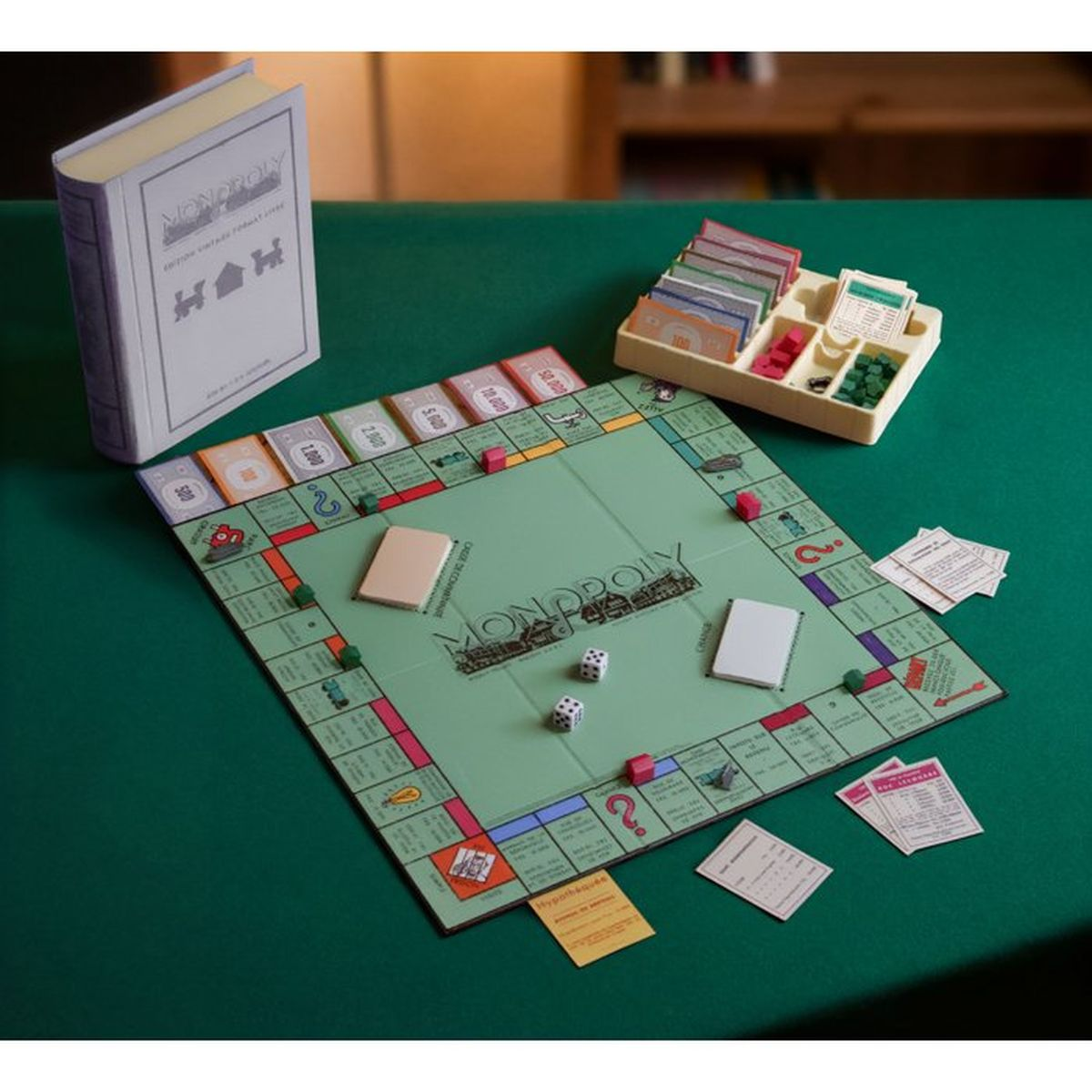 Ein Monopoly-Spielbrett in Retro-Optik mit Würfeln, Geld und einem Buchkarton auf grünem Tisch.