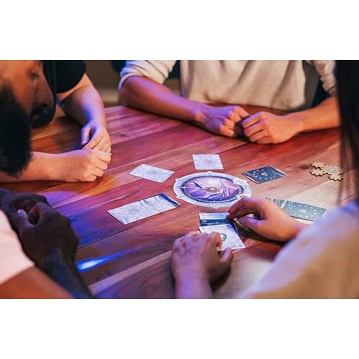 Vier Personen versammeln sich um einen Holztisch und spielen ein Kartenspiel mit runden Brettern.