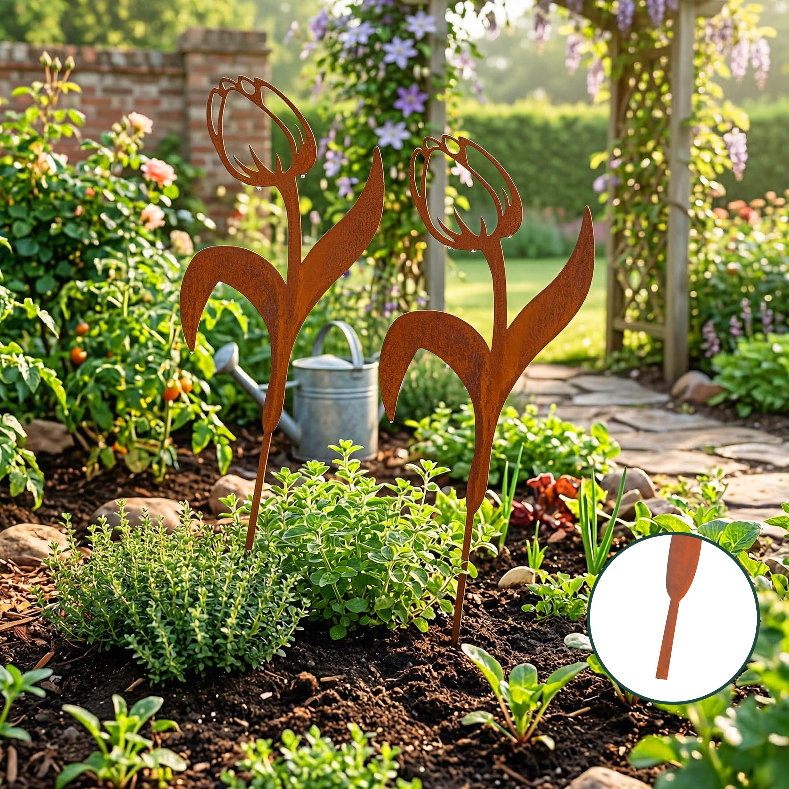 Zwei rostige Metall-Tulpen stecken in einem Gartenbeet mit Blumen, Pflanzen und einer Gießkanne im Hintergrund.