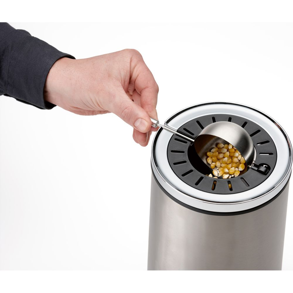 Una mano usa un cucchiaio di metallo per aggiungere mais in una macchina per popcorn in acciaio inossidabile.