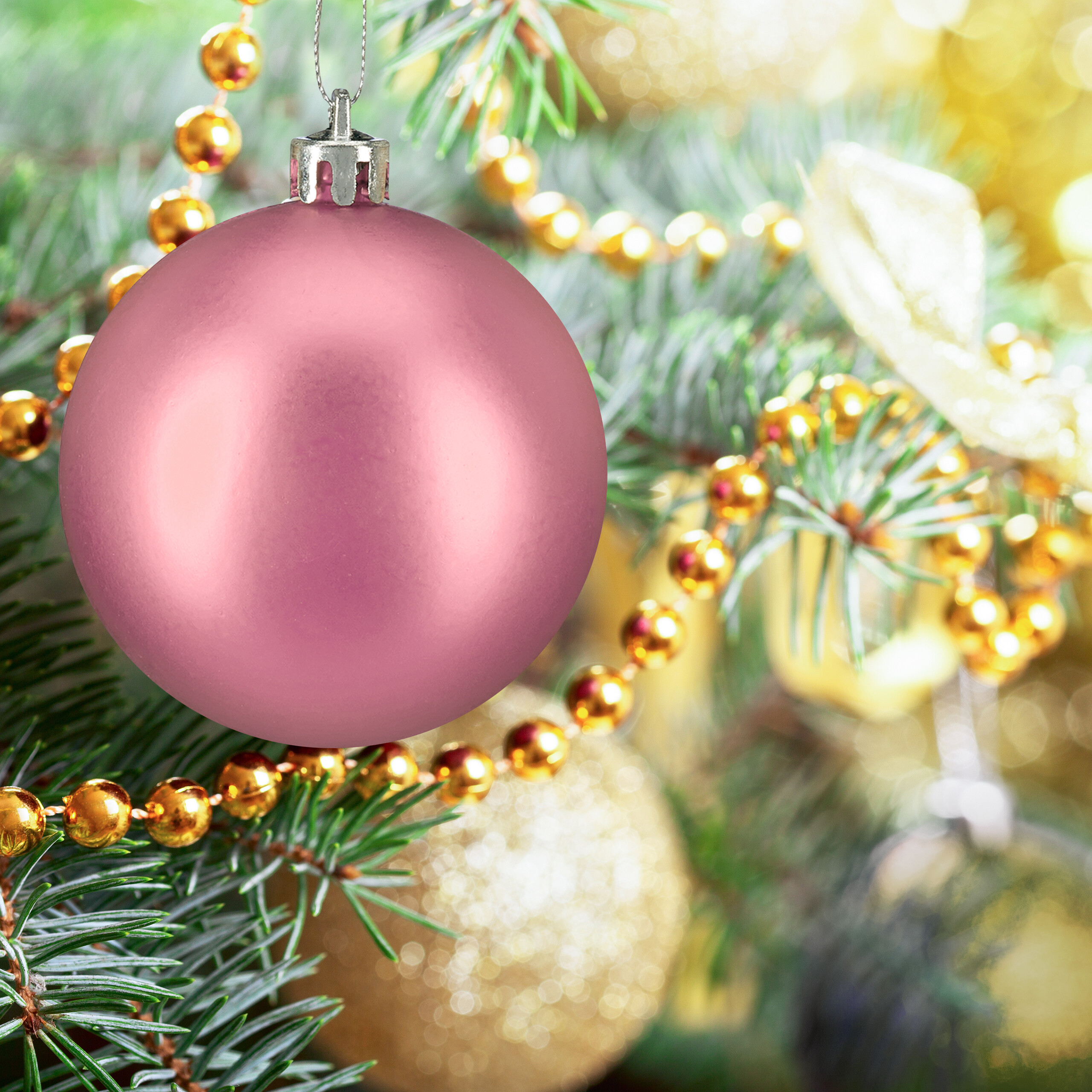 Eine matte rosa Weihnachtskugel hängt an einem Tannenbaum mit goldenen Perlenketten und Lichtern.