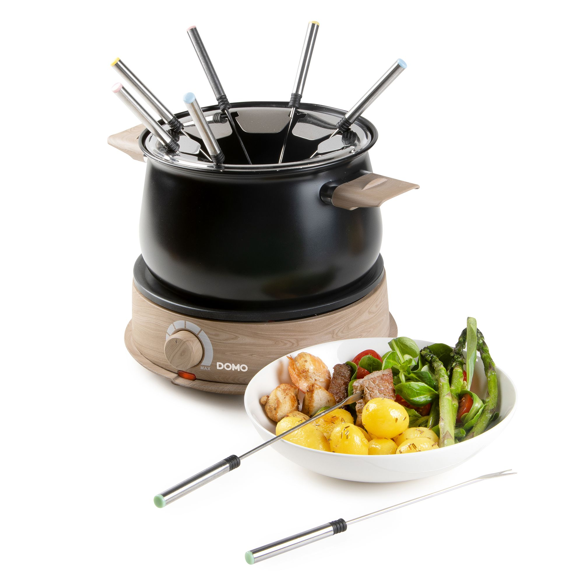 Un caquelon à fondue noir sur socle en bois avec fourchettes, à côté d'un bol de pommes de terre, viande et asperges.