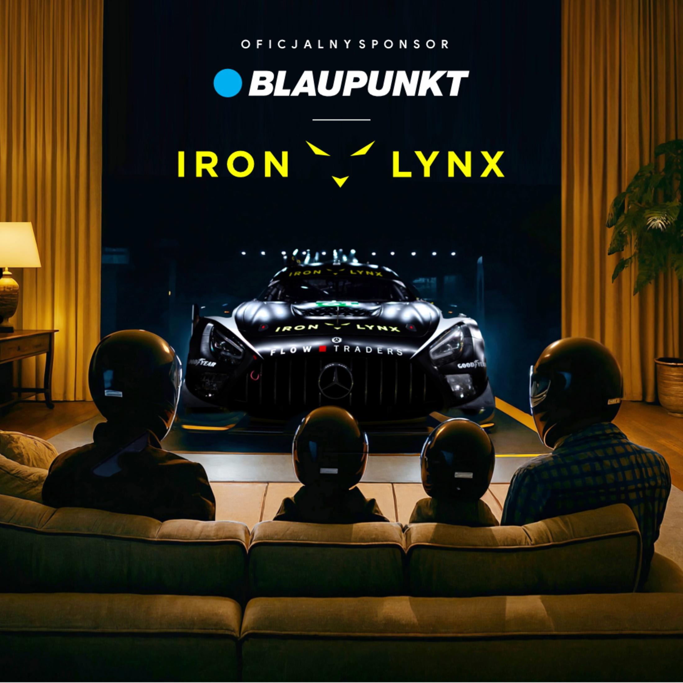 Cztery osoby w kaskach siedzą na kanapie i oglądają samochód wyścigowy na ekranie.
