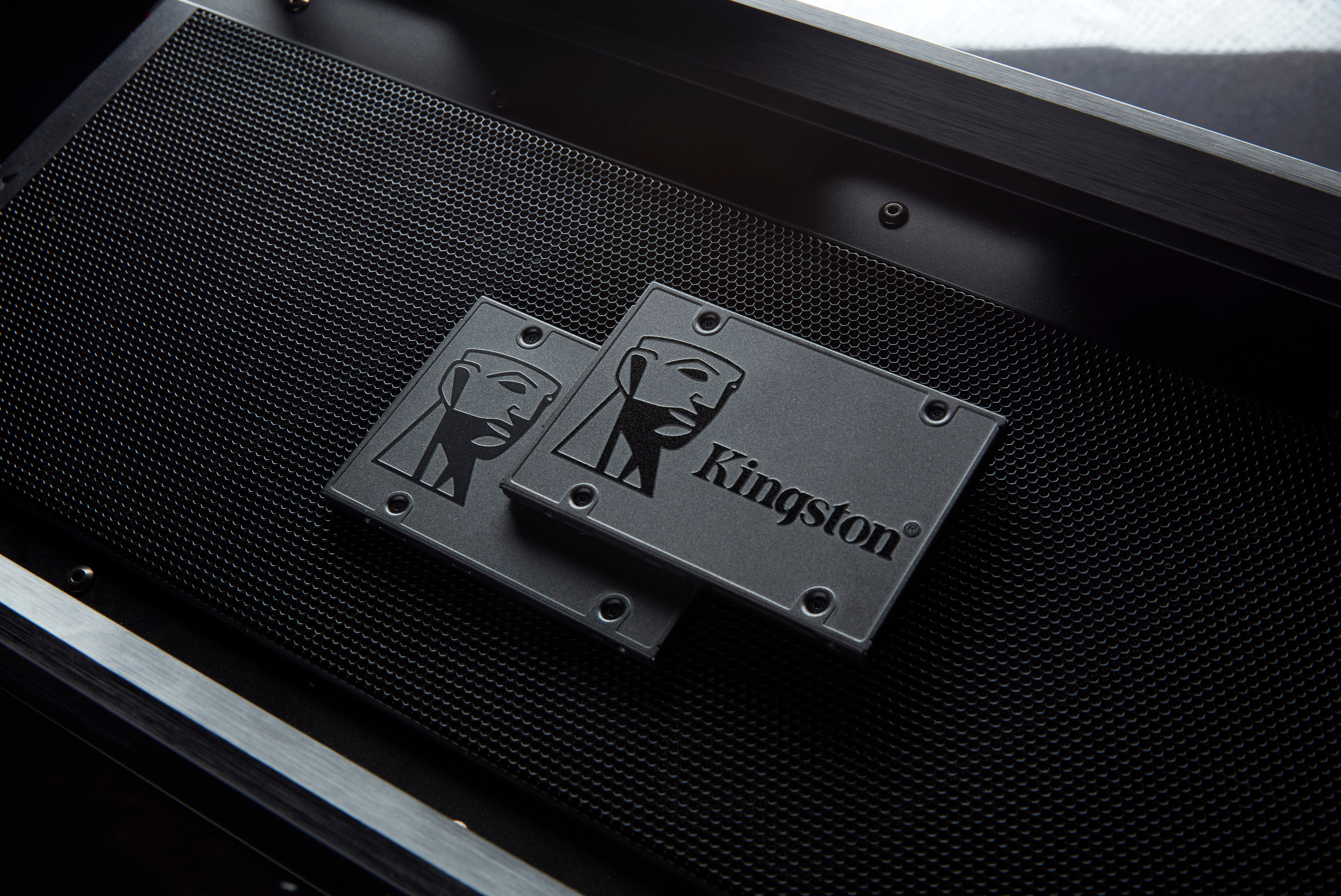 Zwei schwarze Kingston SSDs mit stilisiertem Gesichtslogo liegen auf einer strukturierten Metalloberfläche.