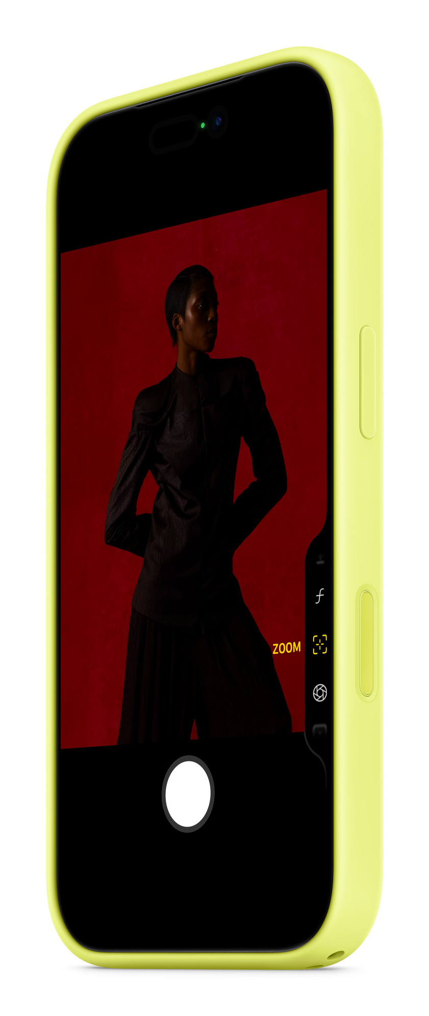 Un teléfono inteligente amarillo brillante muestra una aplicación de cámara con una persona vestida de oscuro sobre un fondo rojo.
