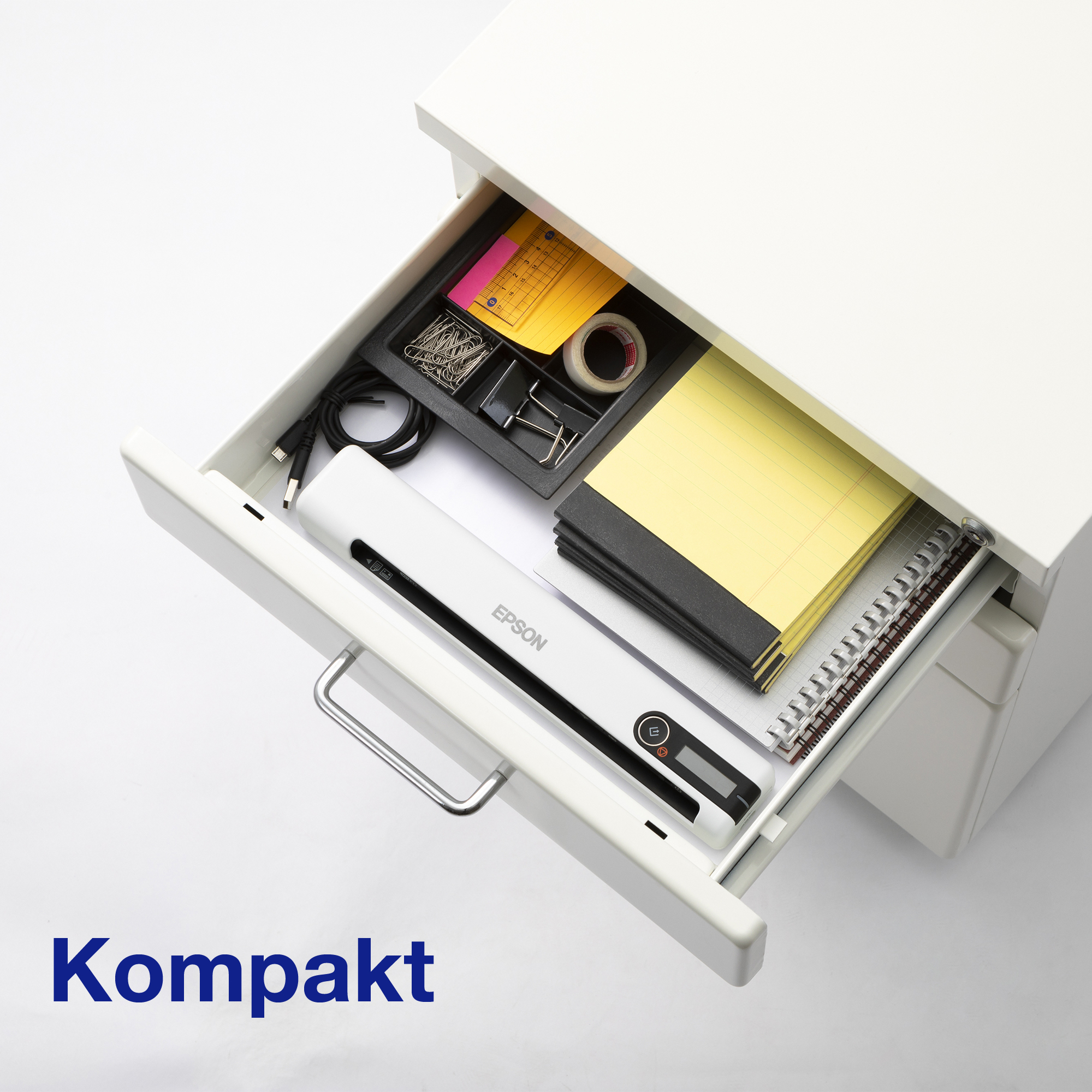 Un tiroir de bureau blanc ouvert contenant un scanner Epson, des blocs-notes et des trombones.