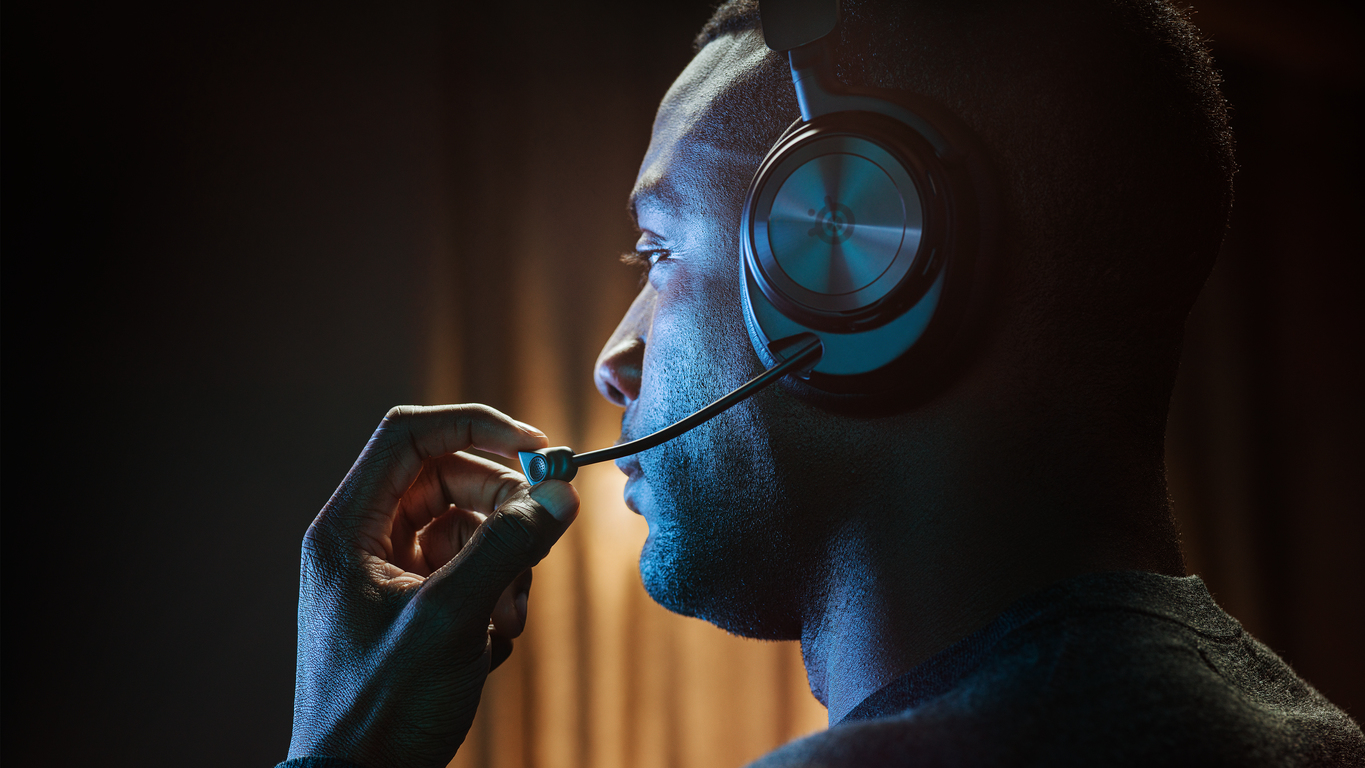 Un hombre con auriculares para juegos y micrófono en una habitación tenue con luz azul.