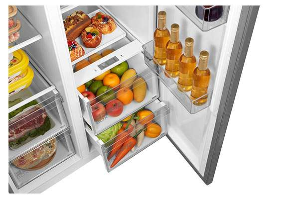 Un refrigerador abierto con estantes llenos, cajones de frutas, botelleros en la puerta y comida fresca.