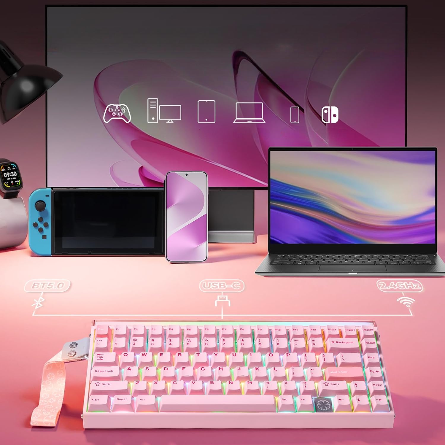 Różowa klawiatura na pierwszym planie, w tle monitor, laptop, konsola, smartfon i smartwatch.