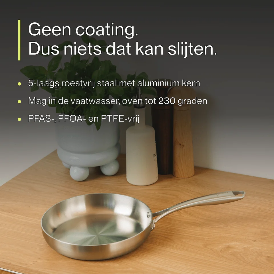 A stainless steel frying pan on a wooden table with Dutch text and kitchen items in the background.