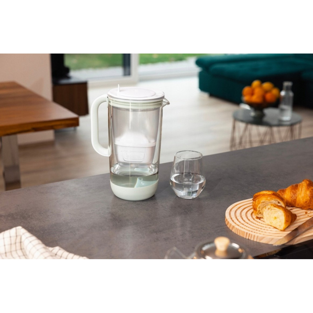 Ein Wasserfilter und ein Glas Wasser stehen auf einer Küchenzeile, im Hintergrund sieht man ein Wohnzimmer.