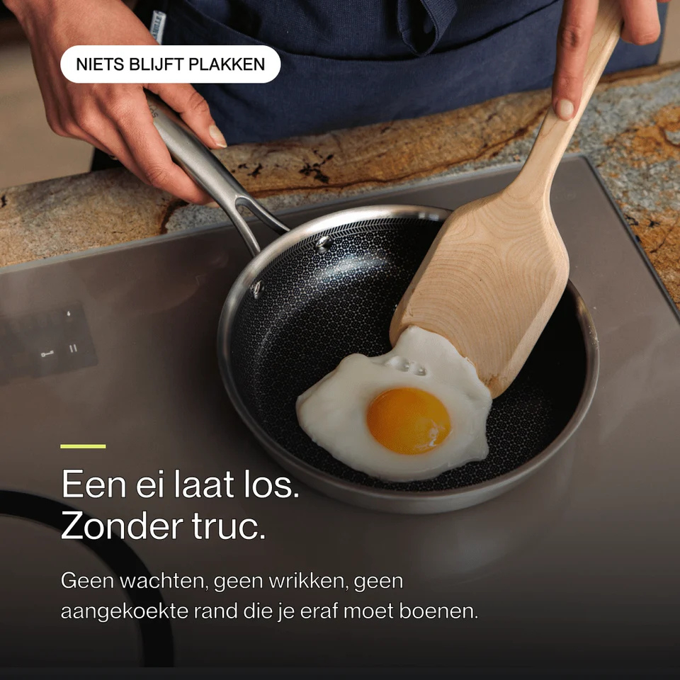 A fried egg is being lifted with a wooden spatula in a textured non-stick pan on a stovetop.
