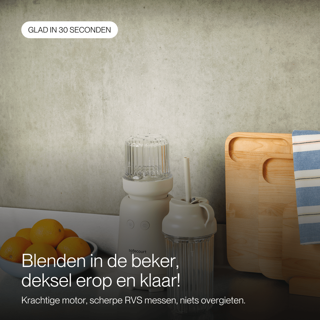 Un blender beige avec tasse de voyage, bol d'oranges et planches à découper en bois contre un mur texturé.