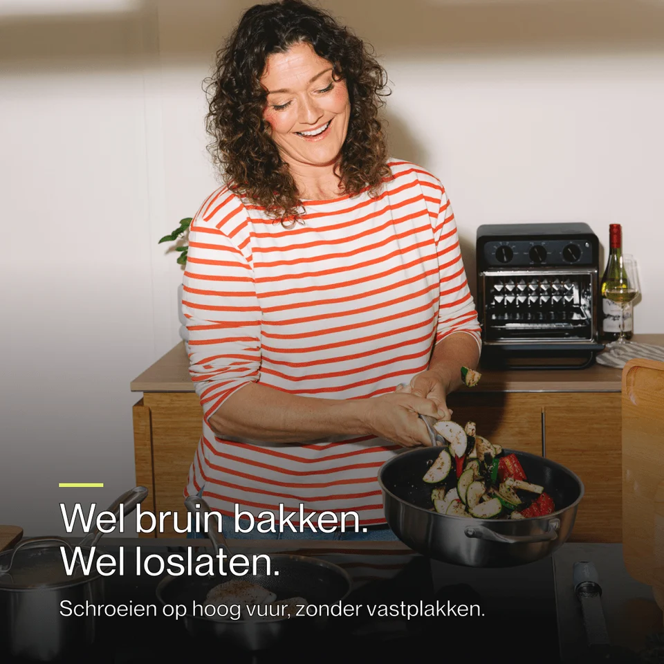 A smiling woman in a red-and-white striped shirt cooks, tossing vegetables in a pan.