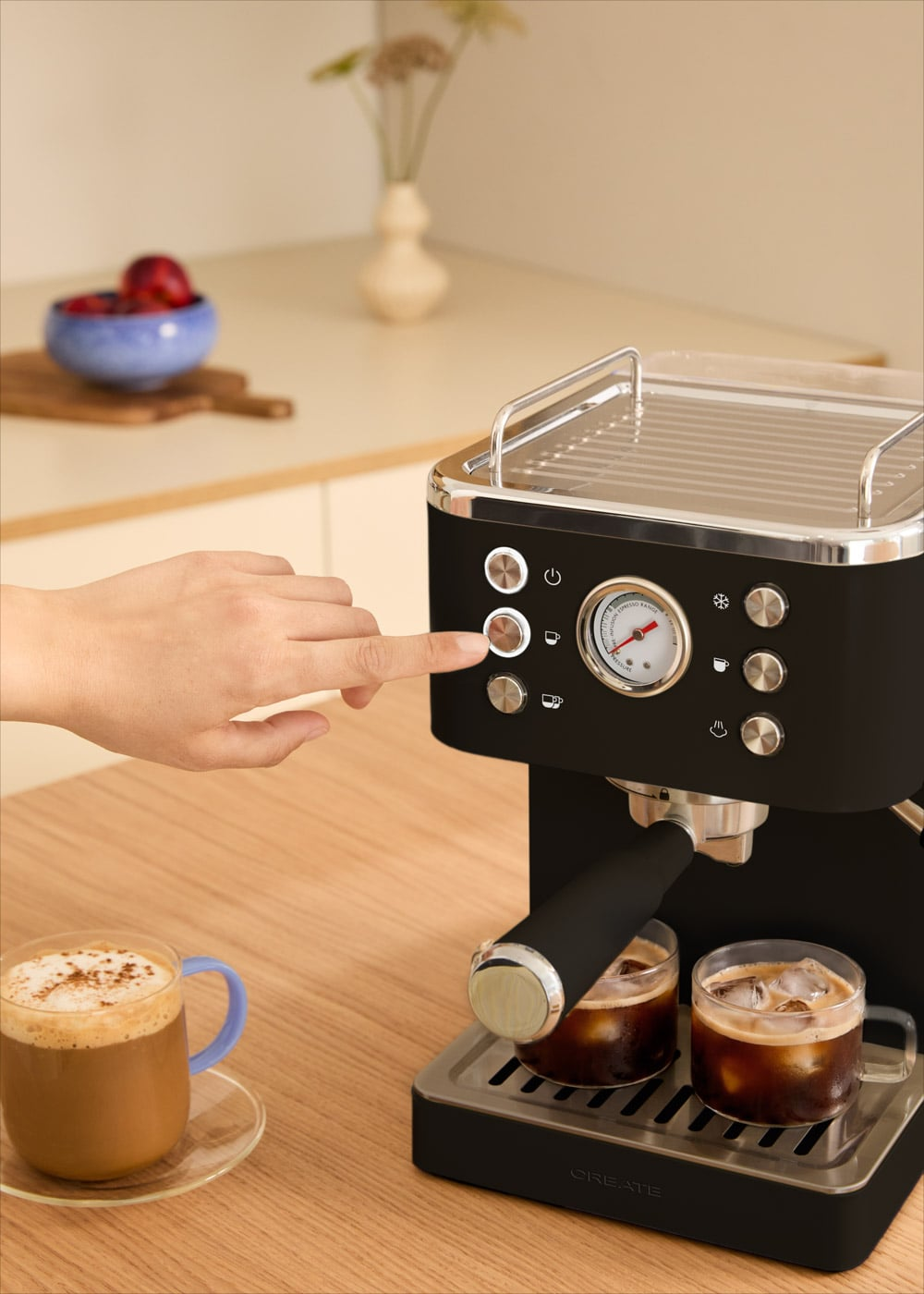 Mano presionando botón en cafetera negra con dos tazas de café en mesa de madera.