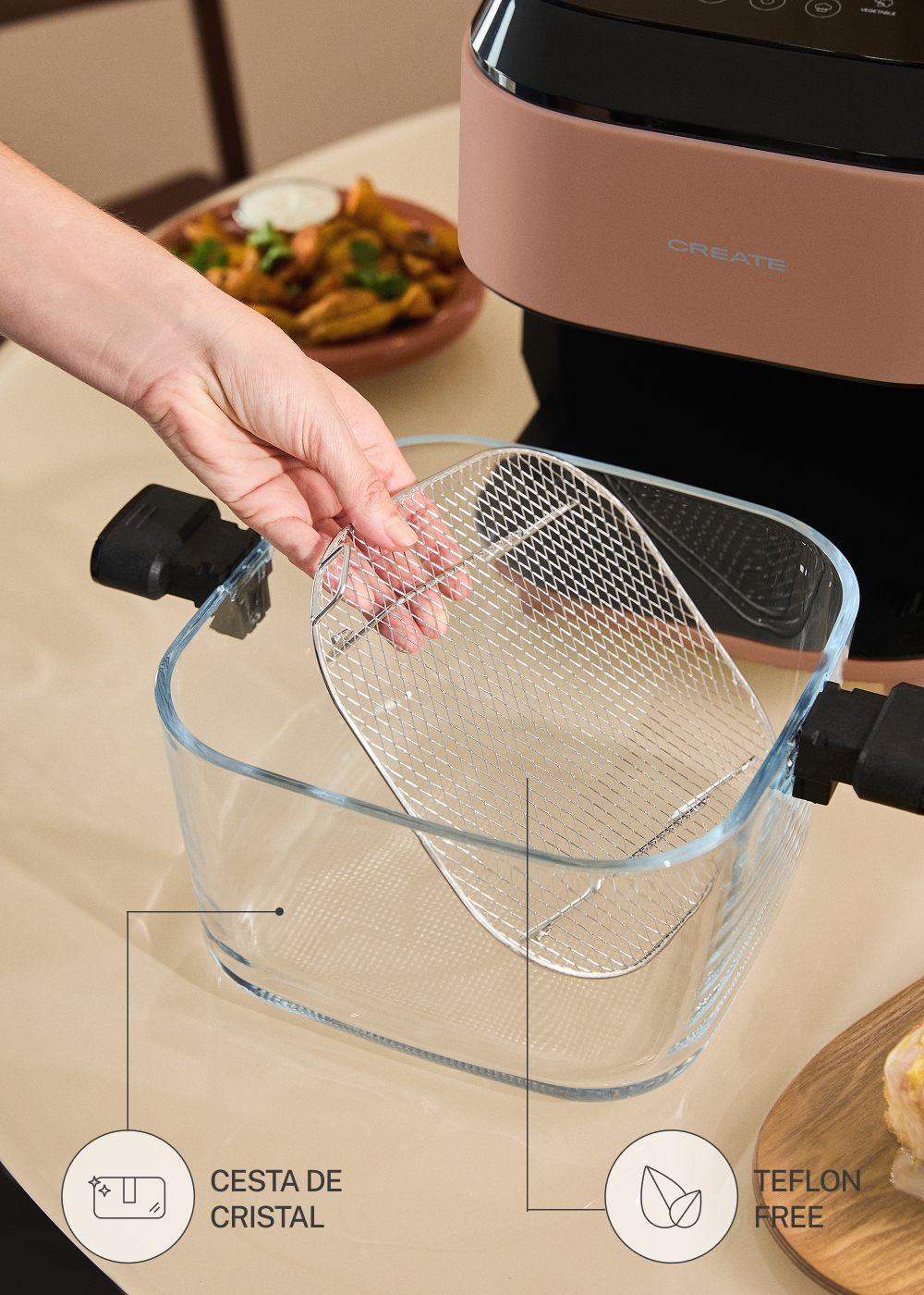 Una mano coloca una rejilla metálica en el recipiente de cristal de una freidora de aire rosa.