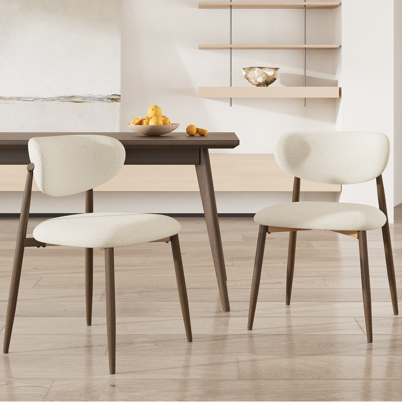 Due sedie imbottite color crema con gambe in legno scuro sono a un tavolo da pranzo con una ciotola di arance.