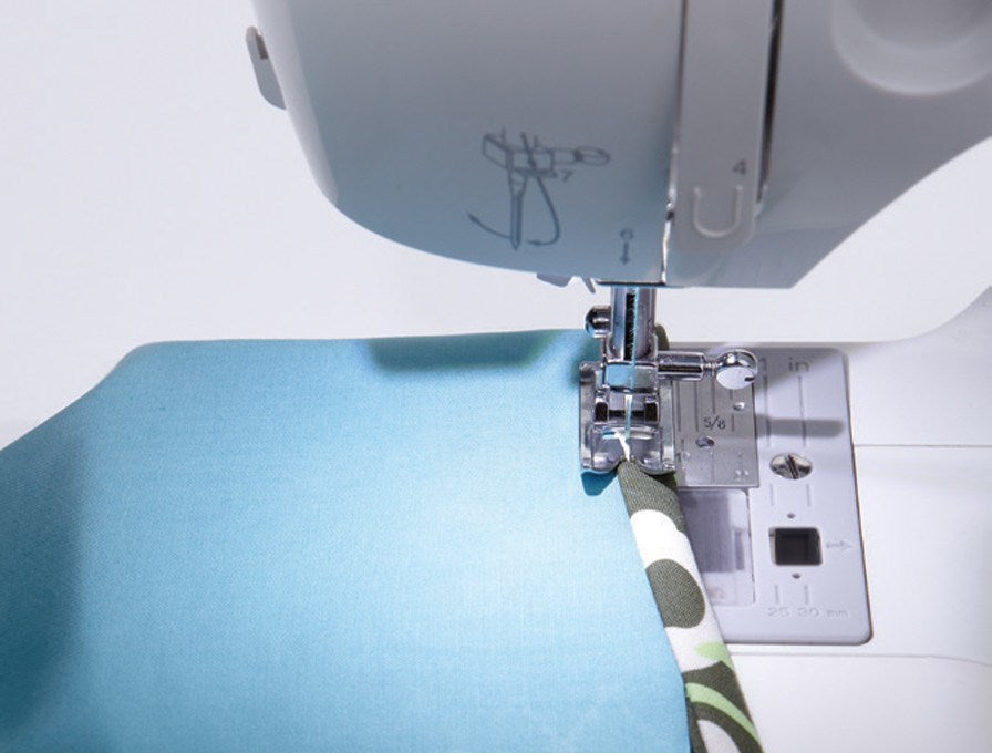 Nähmaschine verbindet blauen und camo-gemusterten Stoff unter der silbernen Nadel.