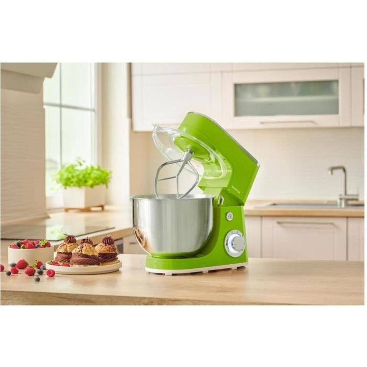 Un'impastatrice verde su un bancone di legno in una cucina luminosa, con dolcetti e bacche vicini.