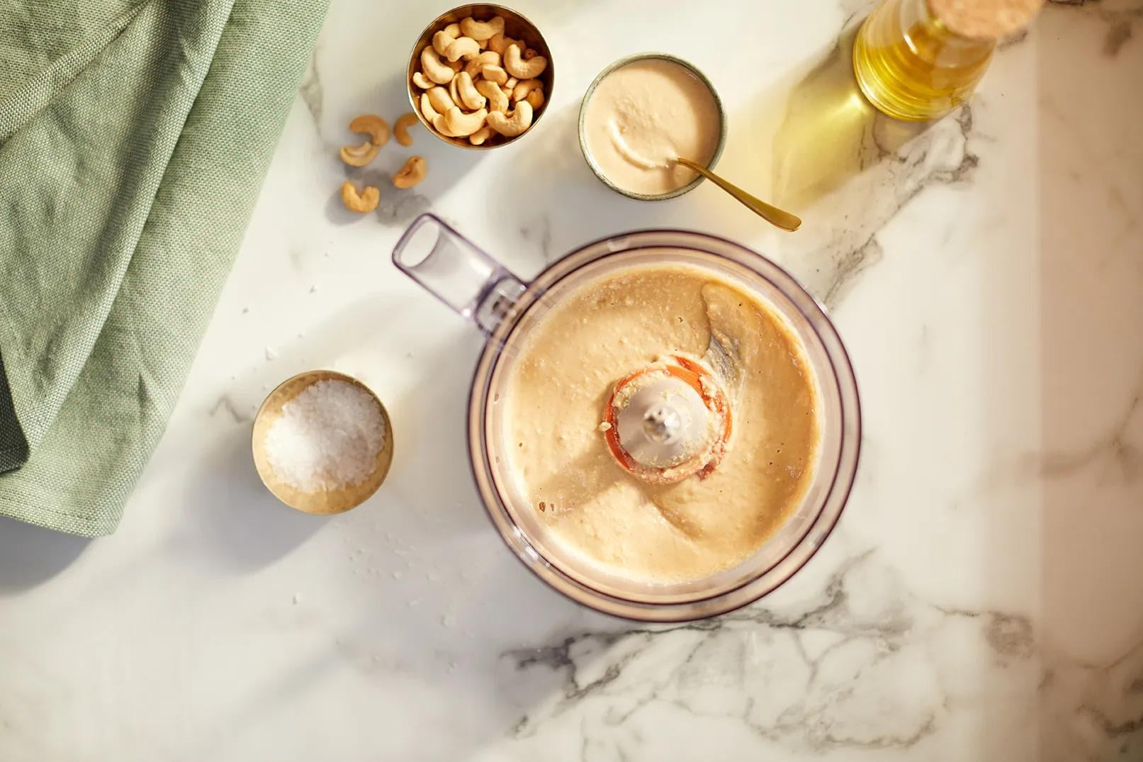 Mixer auf Marmorplatte mit Cashews, Salz, Öl und einer cremigen Paste.