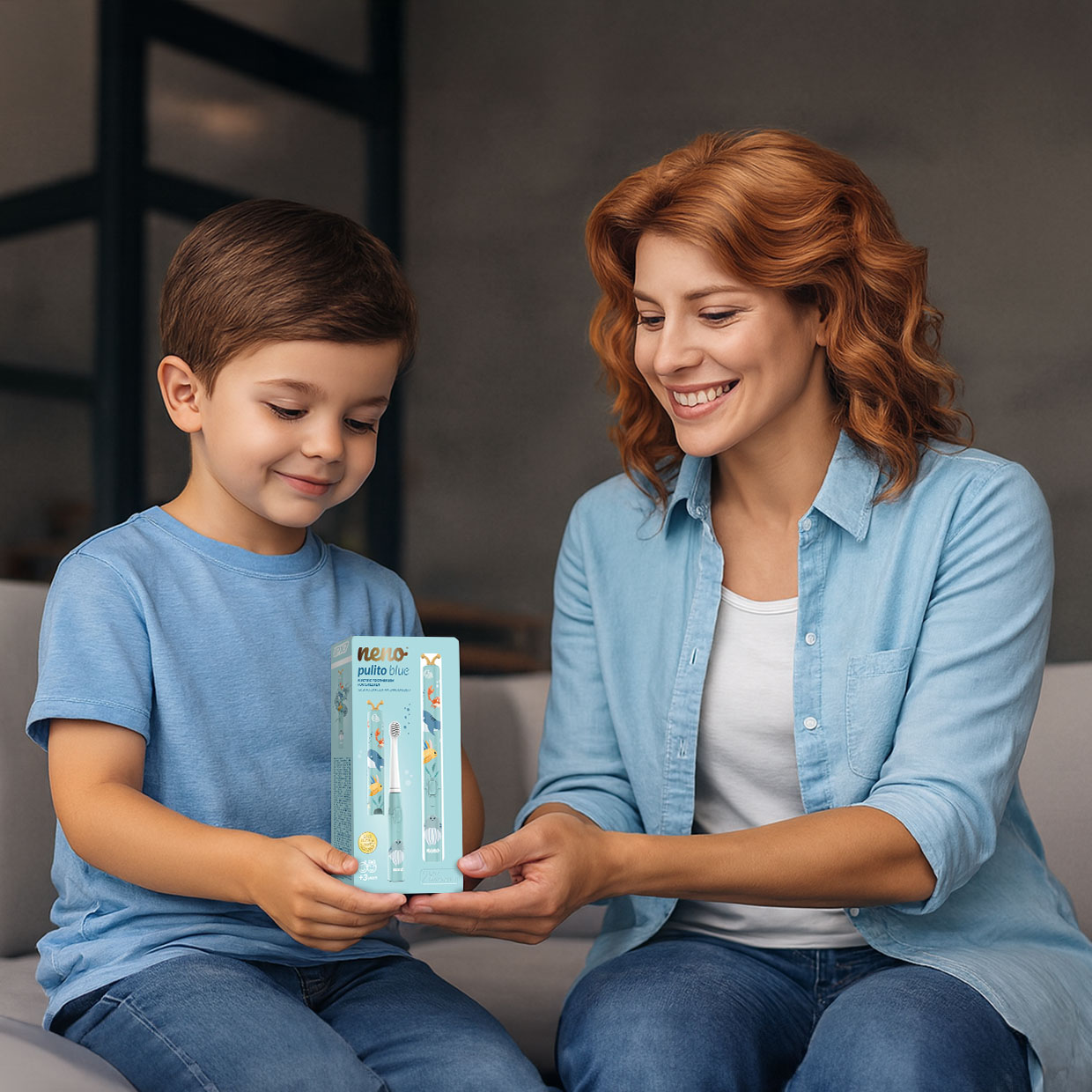 Eine lächelnde Mutter und ihr Sohn sitzen auf einem Sofa und halten gemeinsam eine blaue Produktbox.