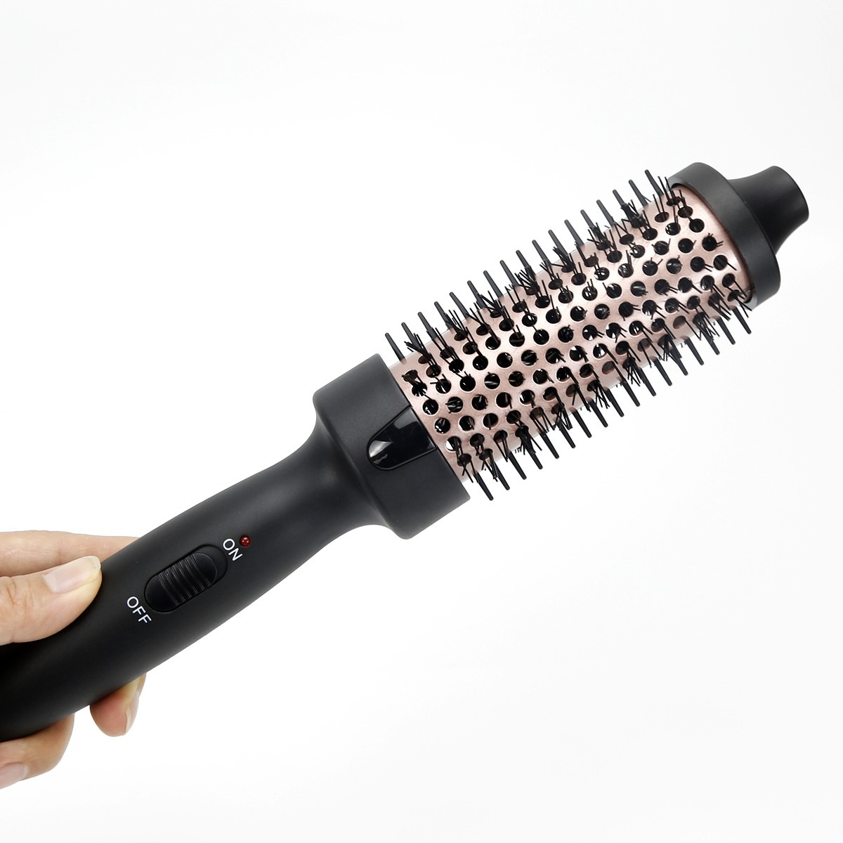 Una mano sostiene un moldeador de cabello negro con accesorio de cepillo redondo dorado contra fondo blanco.