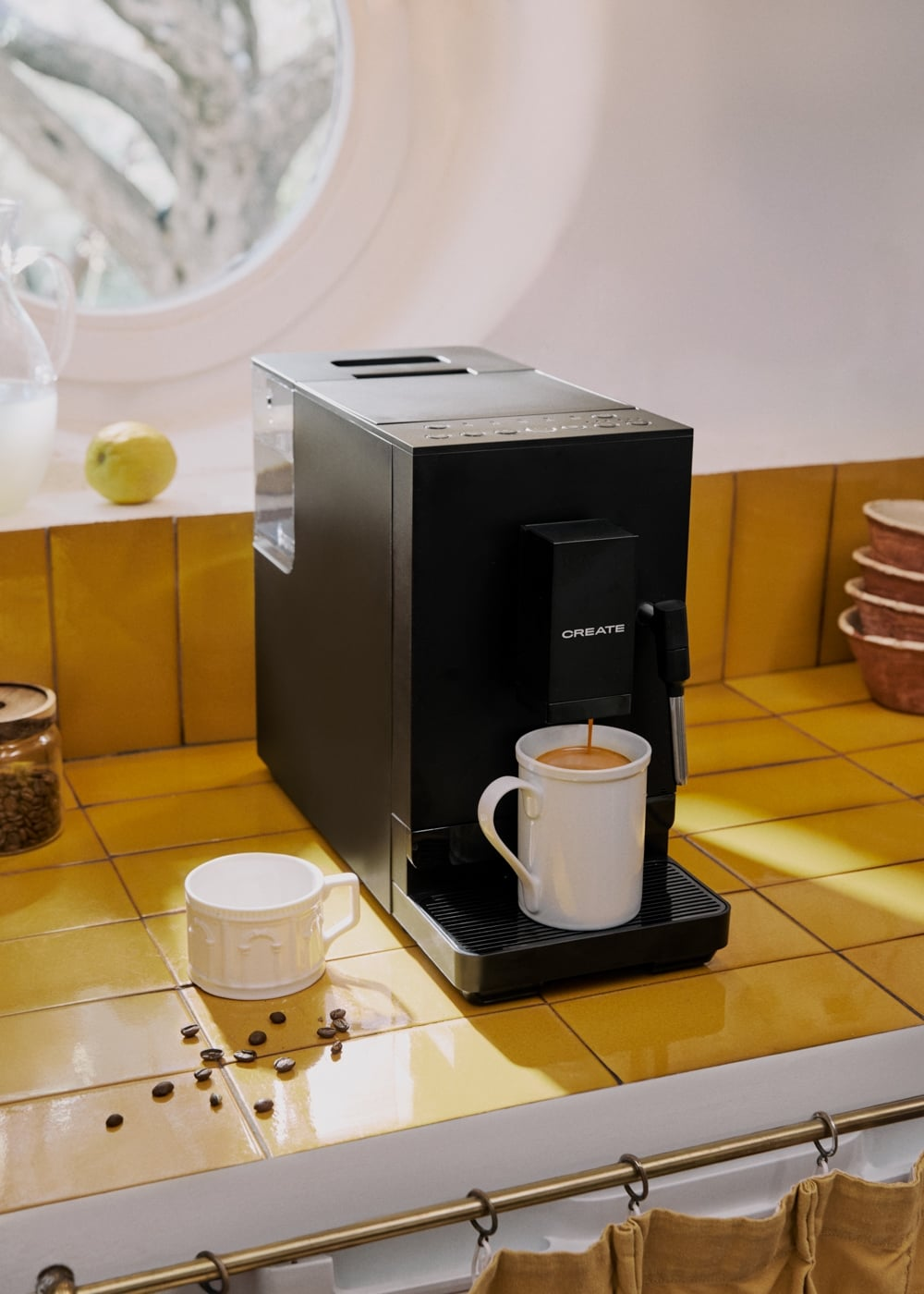 Una cafetera negra sobre azulejos amarillos llena una taza blanca con café.