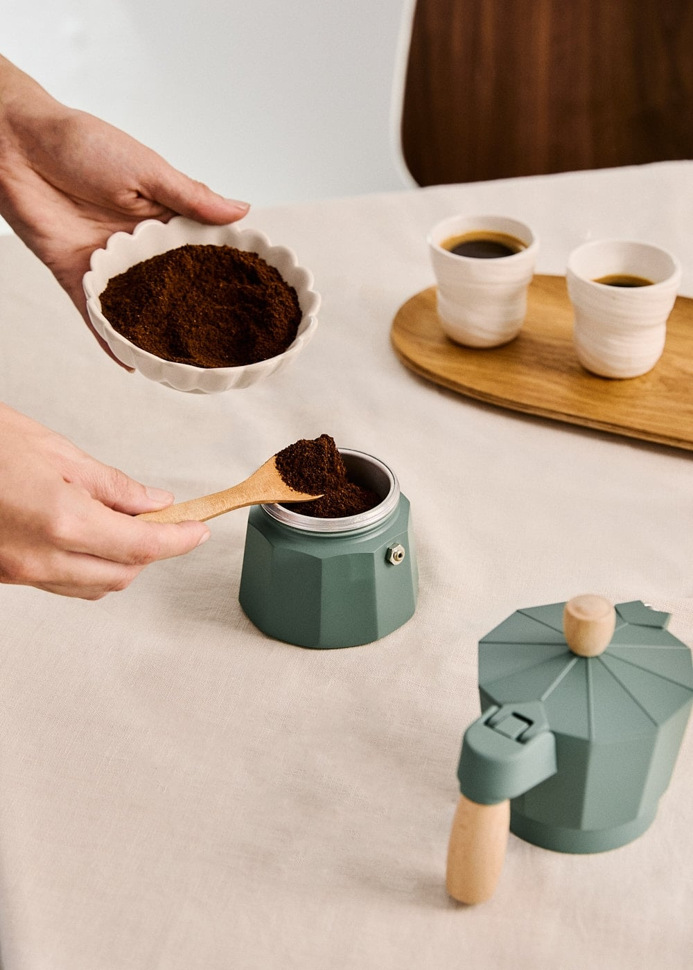Alguien usa una cuchara de madera para echar café molido en una cafetera italiana verde.