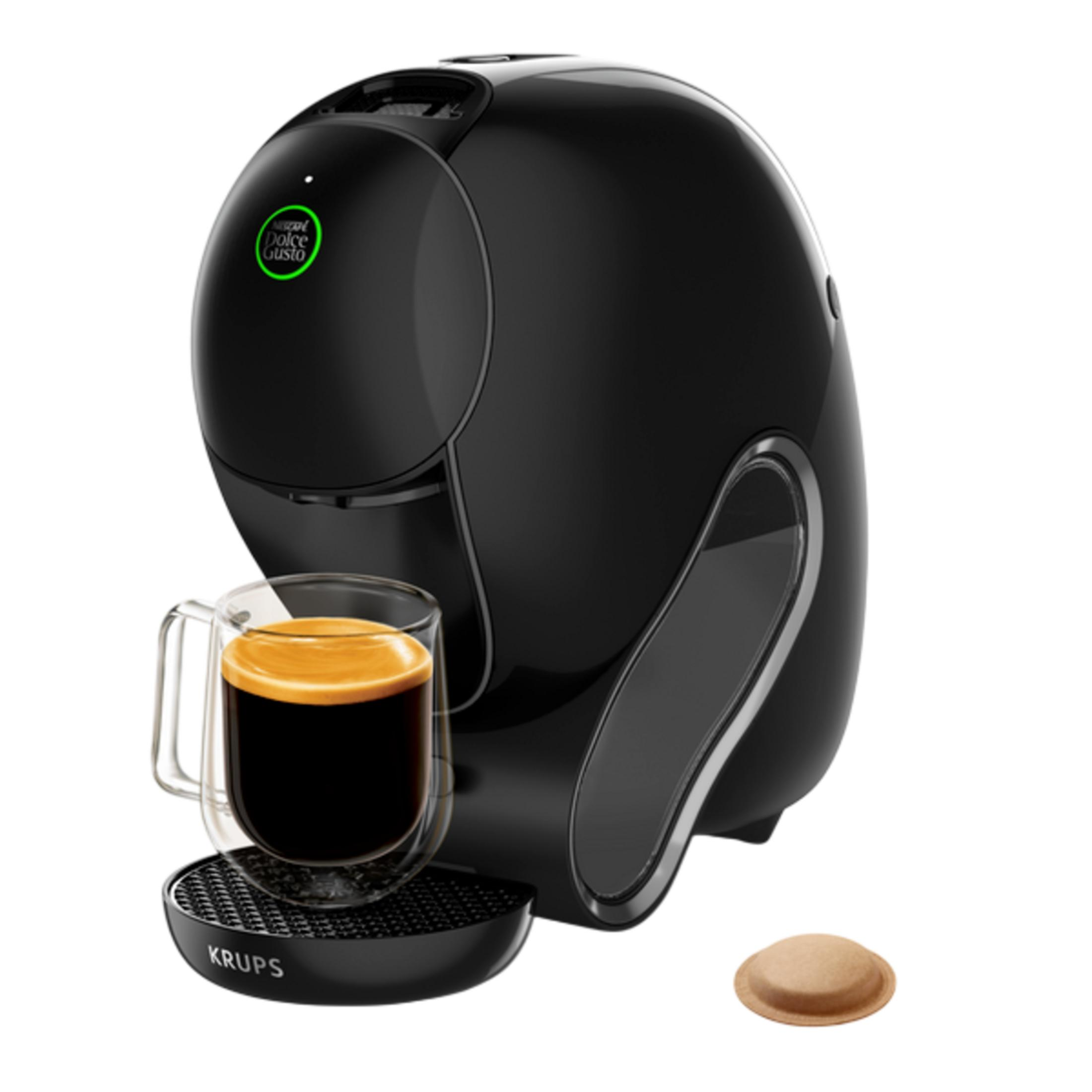Una macchina da caffè Krups nera con una tazza di vetro di caffè e una cialda su sfondo bianco.