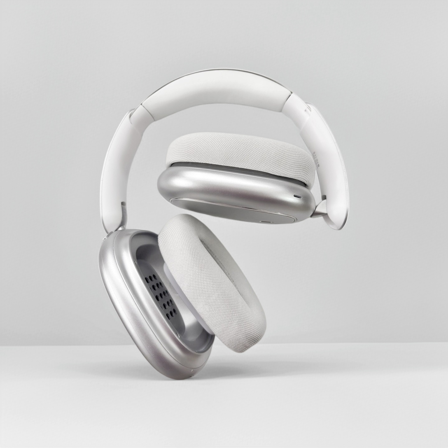 Modernos auriculares plateados con diadema blanca flotan sobre un fondo claro.