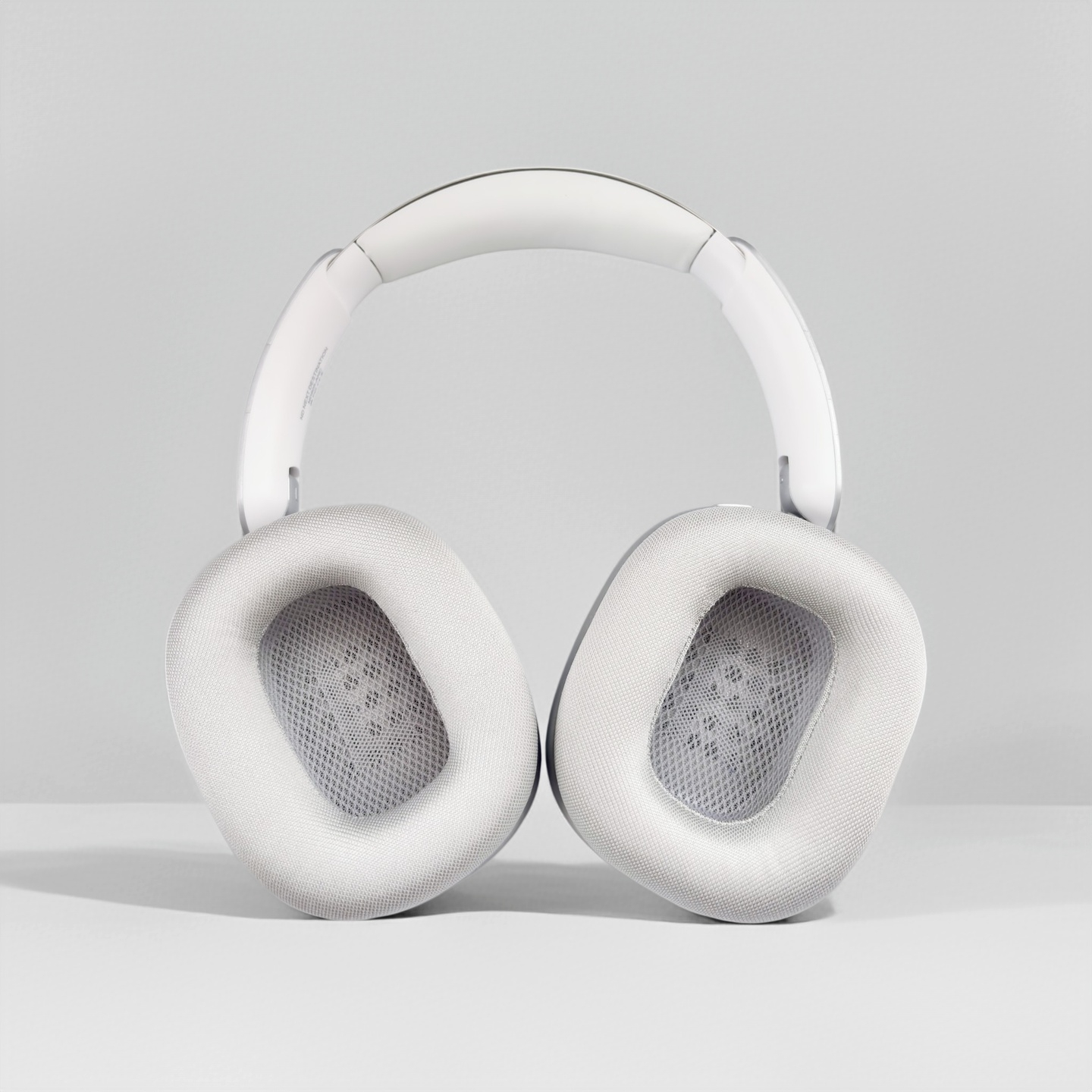 Auriculares supraurales blancos con almohadillas de malla sobre una superficie gris clara y fondo simple.