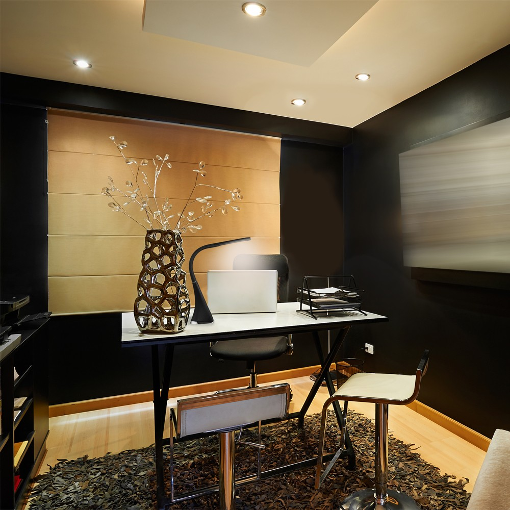 Elegante oficina moderna en casa con paredes oscuras, escritorio claro, jarrón decorativo e iluminación empotrada.