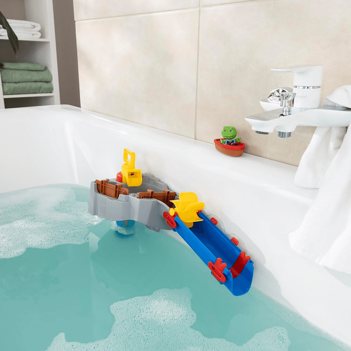 Juguete de baño colorido con tobogán y rueda hidráulica en una bañera con agua azul.