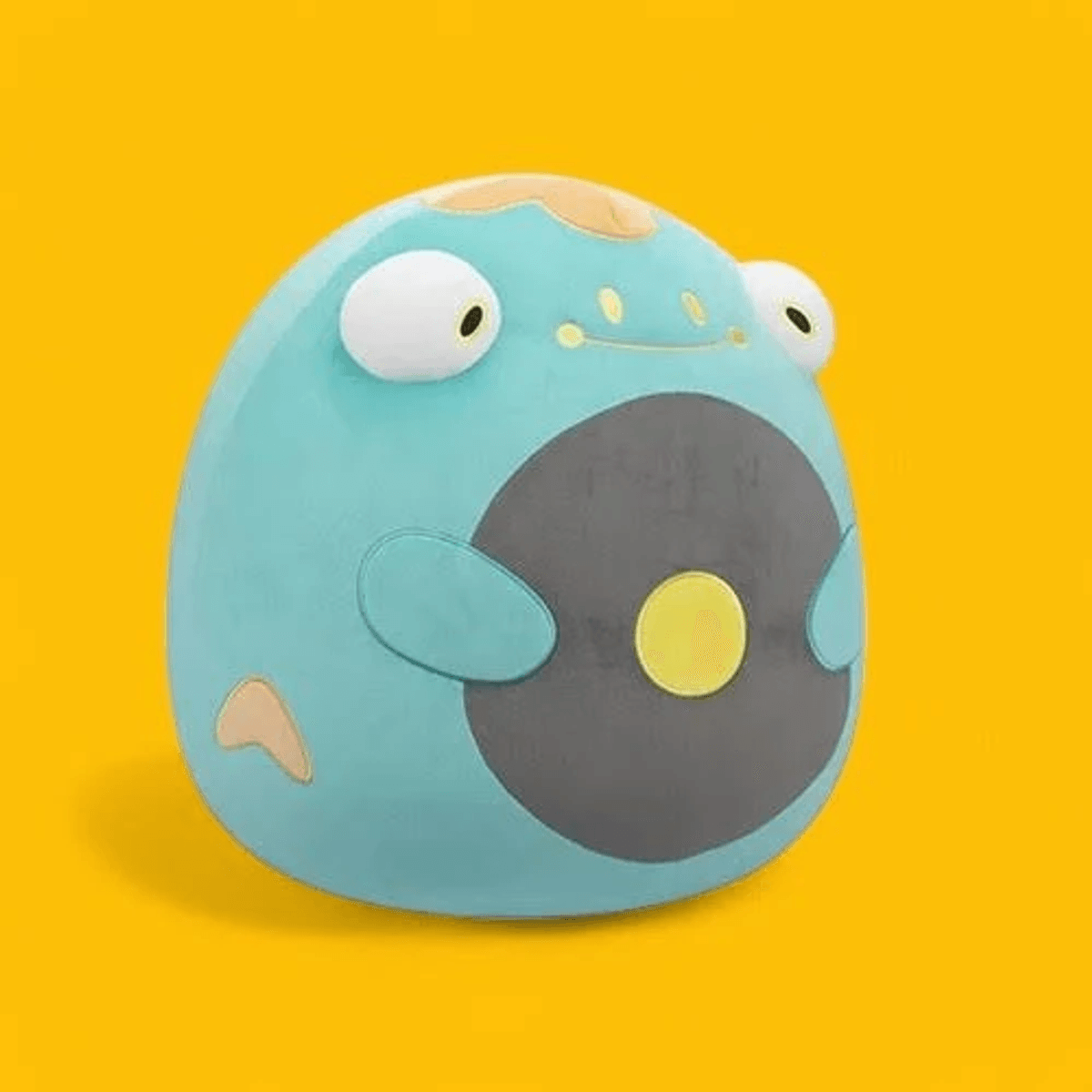 Una rana de peluche redonda y azul con ojos grandes y barriga gris sobre fondo amarillo.