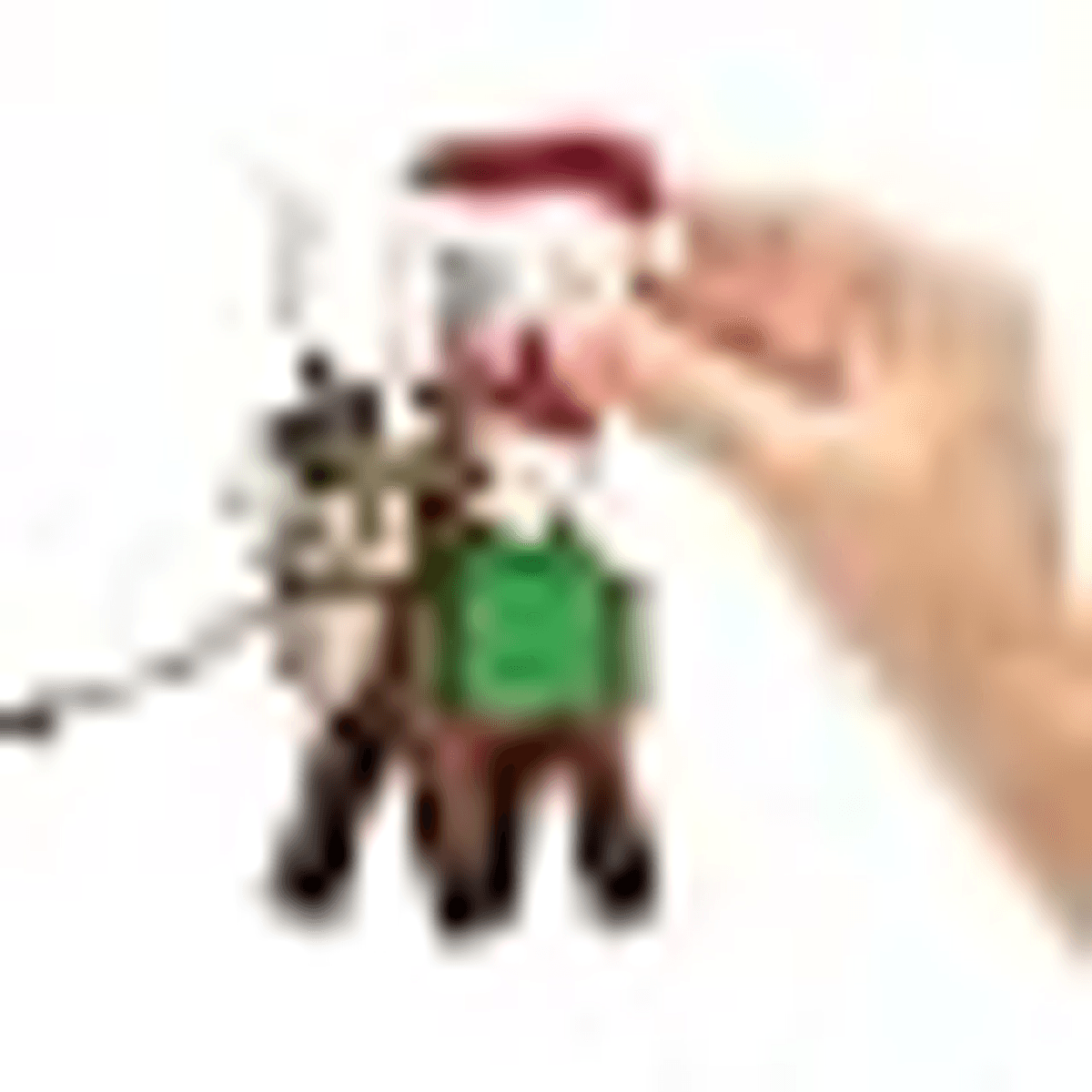 Eine Hand platziert eine kleine Spielfigur mit grünem Rumpf und rotem Hut vor weißem Hintergrund.