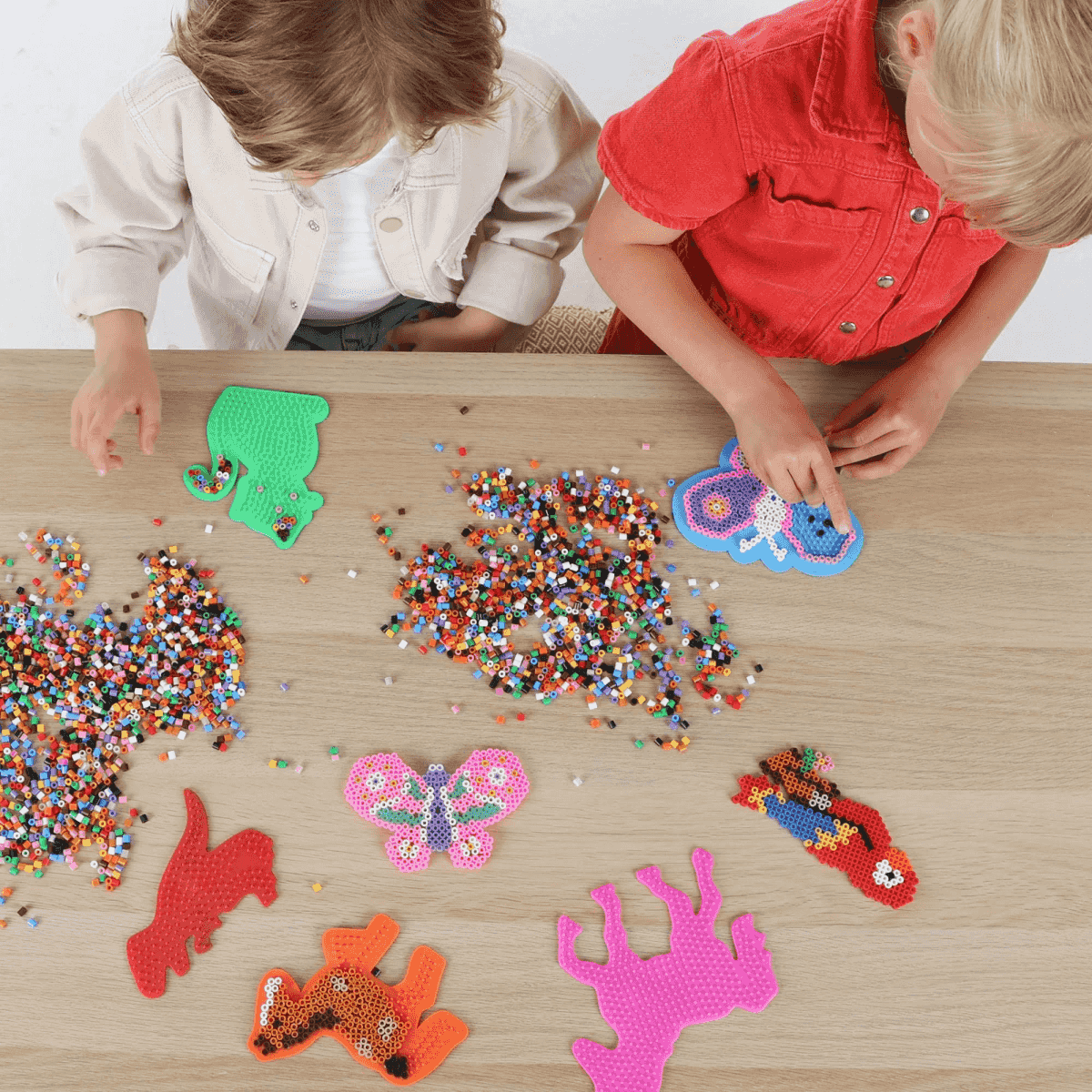 Dos niños elaboran manualidades con cuentas de colores en una mesa.