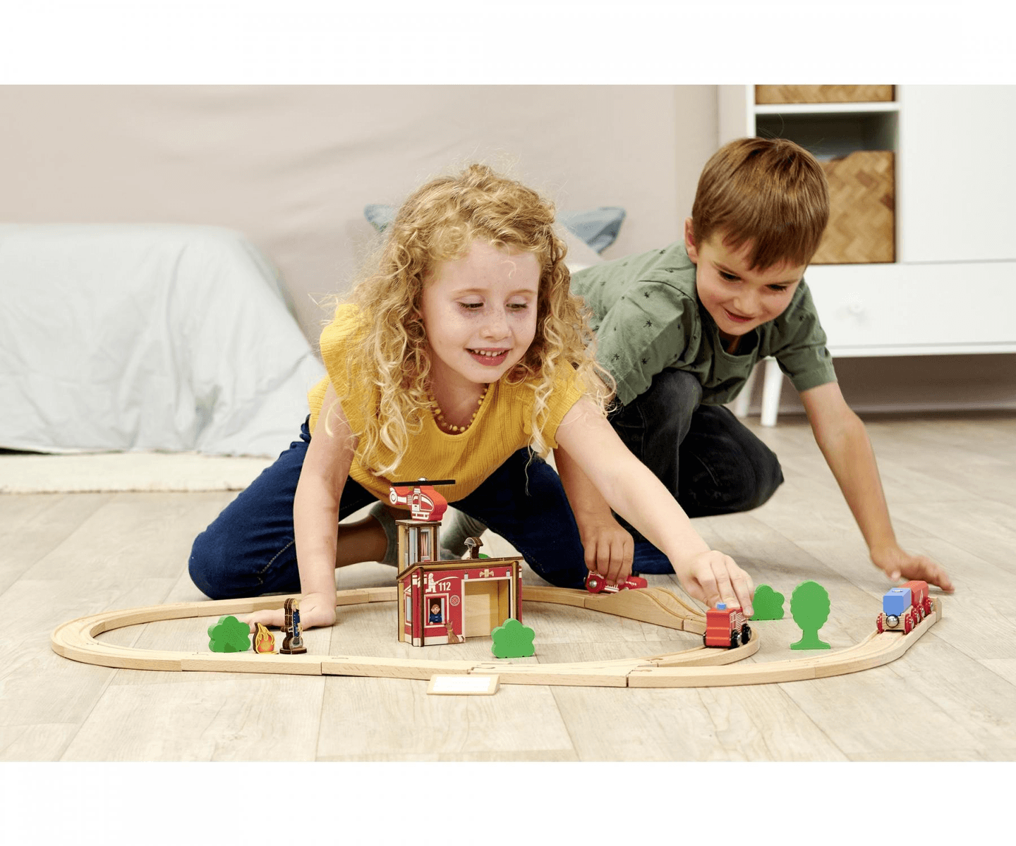 Un niño y una niña juegan felizmente con un tren de juguete de madera en el suelo.