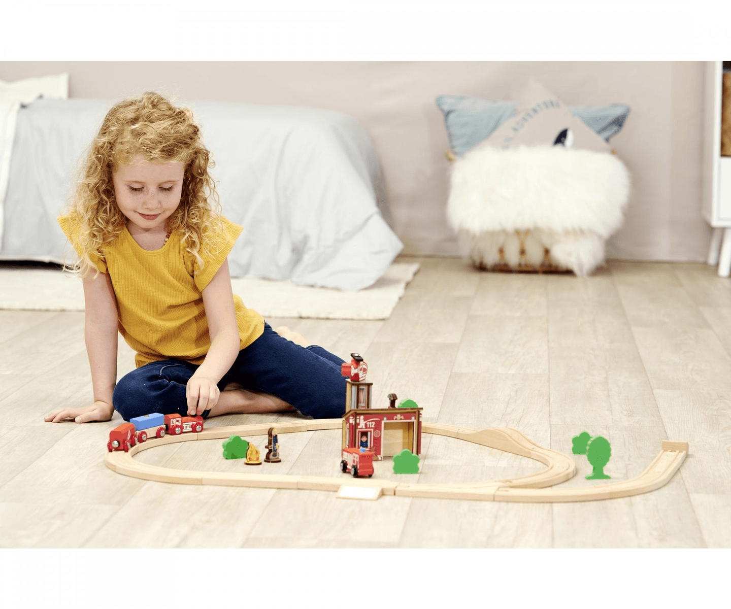 Una niña de pelo rizado está sentada en el suelo jugando con un tren de juguete de madera.