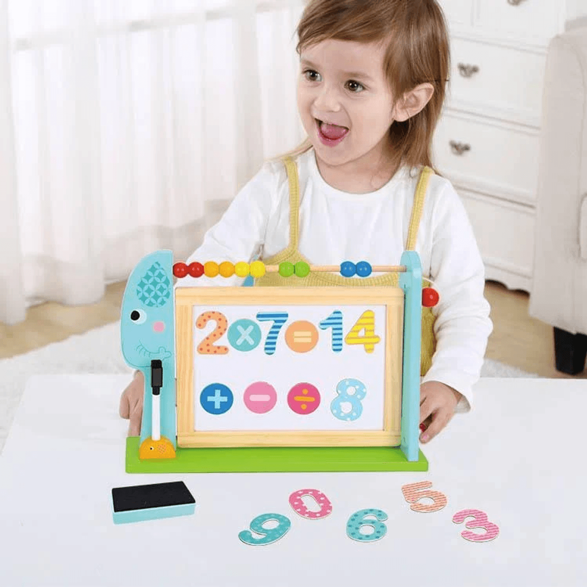 Un niño sonriente juega con un tablero de matemáticas de madera en una mesa blanca.