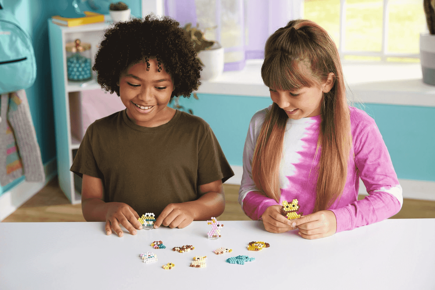 Zwei lächelnde Kinder sitzen am Tisch und spielen mit kleinen bunten Perlenfiguren.
