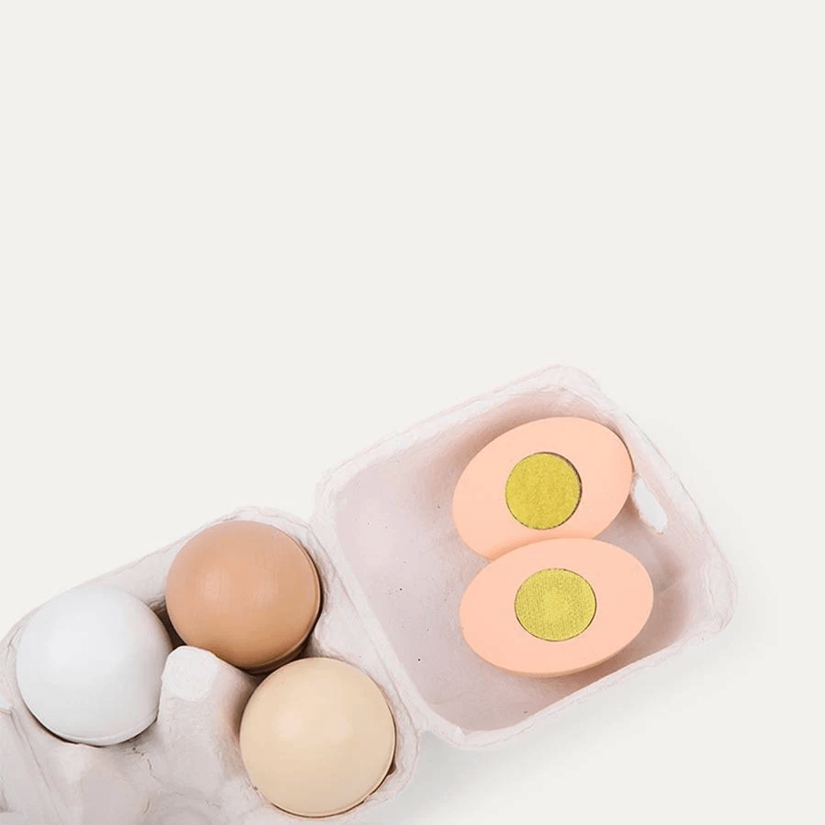 Cartón de huevos con tres huevos de madera enteros en blanco y marrón, más un huevo cortado con yema amarilla.