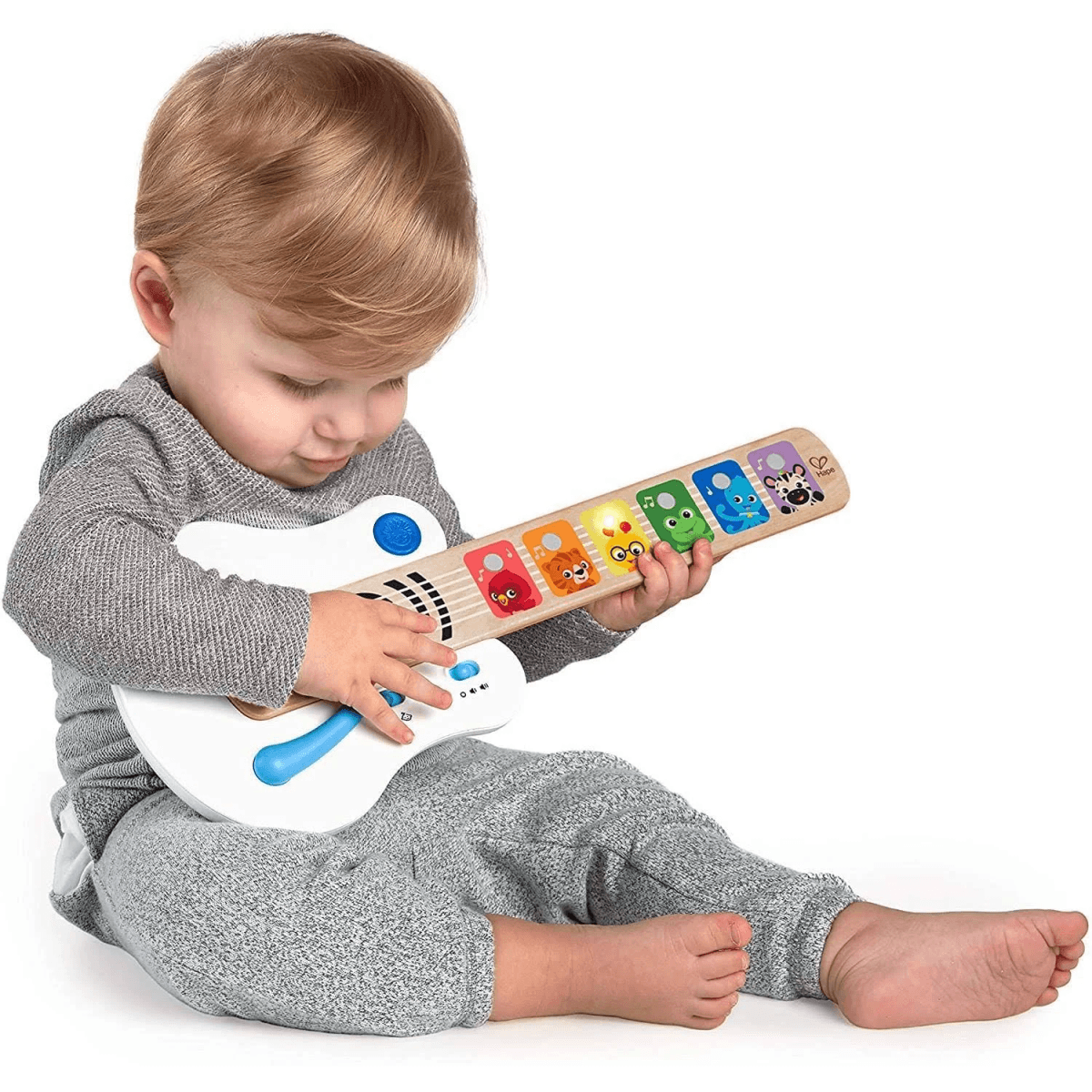 Niño pequeño con jersey gris sentado jugando con una guitarra de juguete de madera.