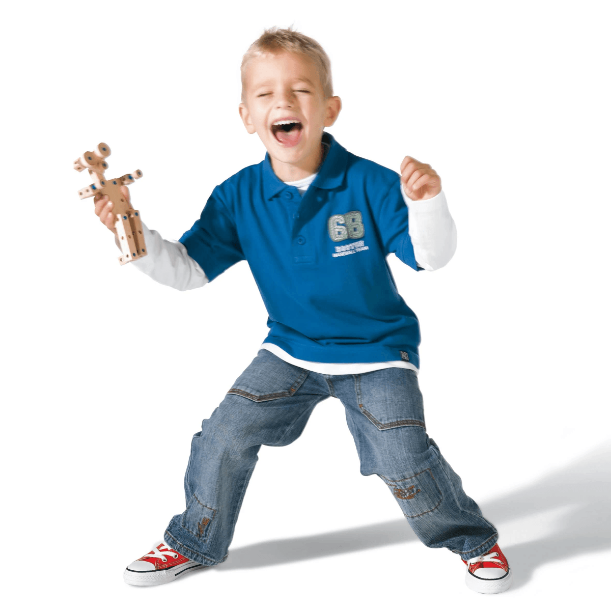 Un niño feliz con polo azul y jeans sostiene un juguete de madera y ríe alegremente.