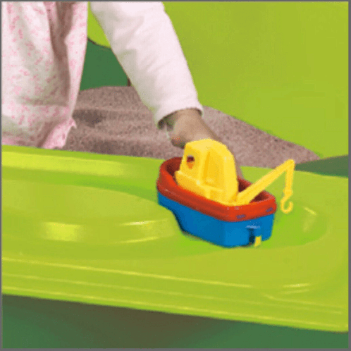 Un niño juega con un barco de juguete colorido en una superficie verde.