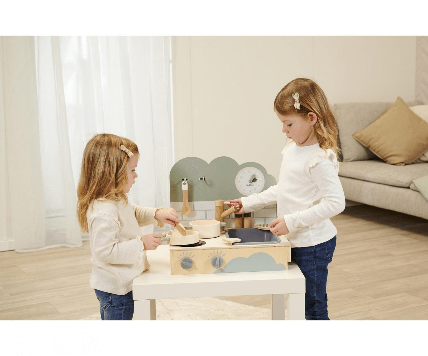 Zwei kleine Mädchen spielen in einem hellen Zimmer an einer kleinen Holzküche.