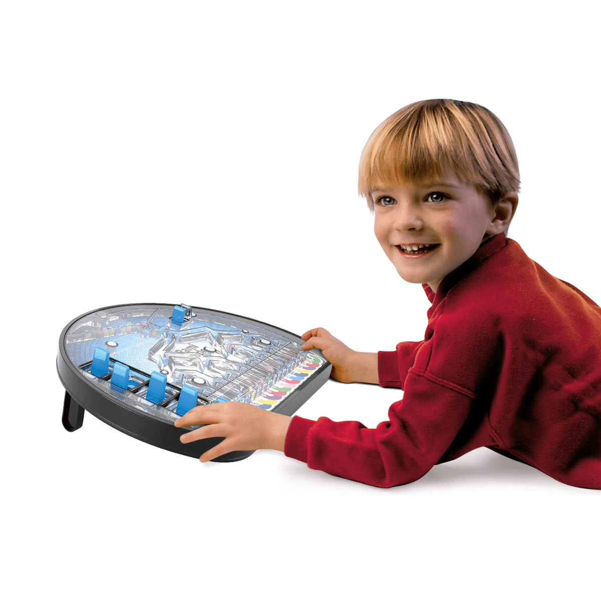 Un niño sonriente con camisa roja está acostado en el piso jugando con un juego de lógica de canicas.