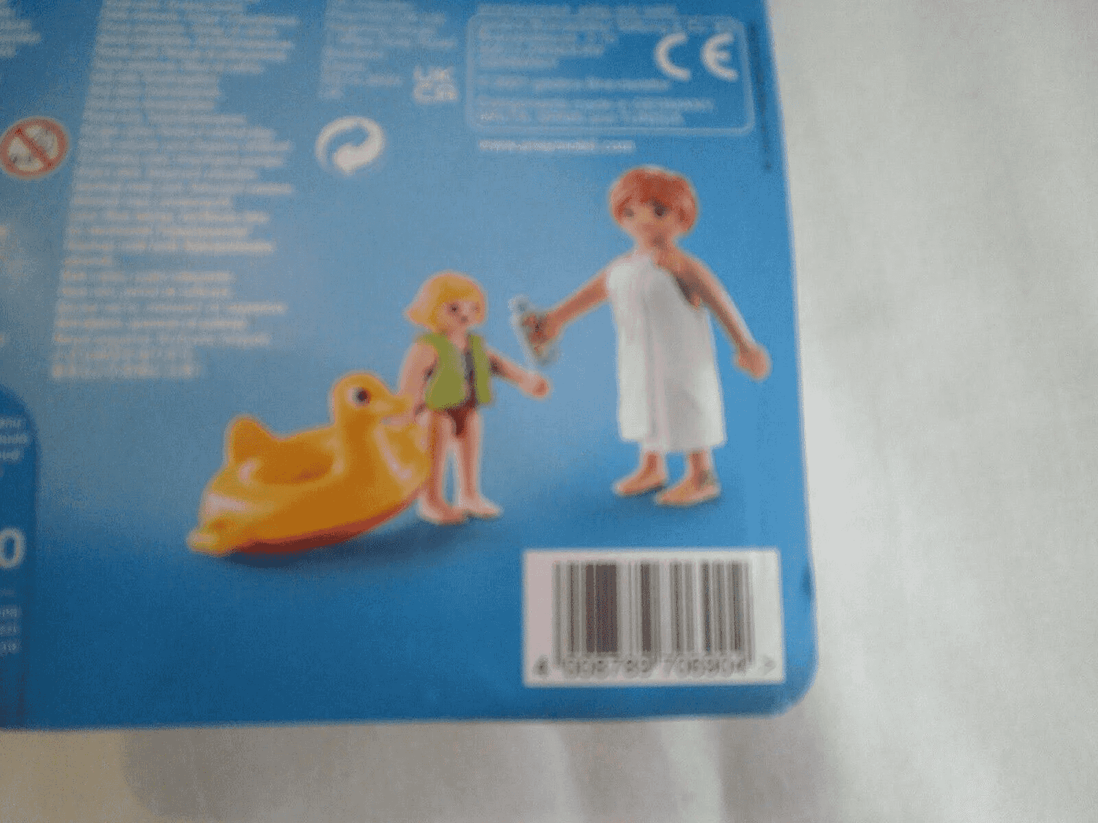 Empaque de Playmobil con una figura en toalla, un niño con flotador de pato y un código de barras.